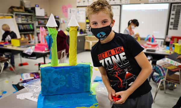 Student holds up a castle made out of recycled materials